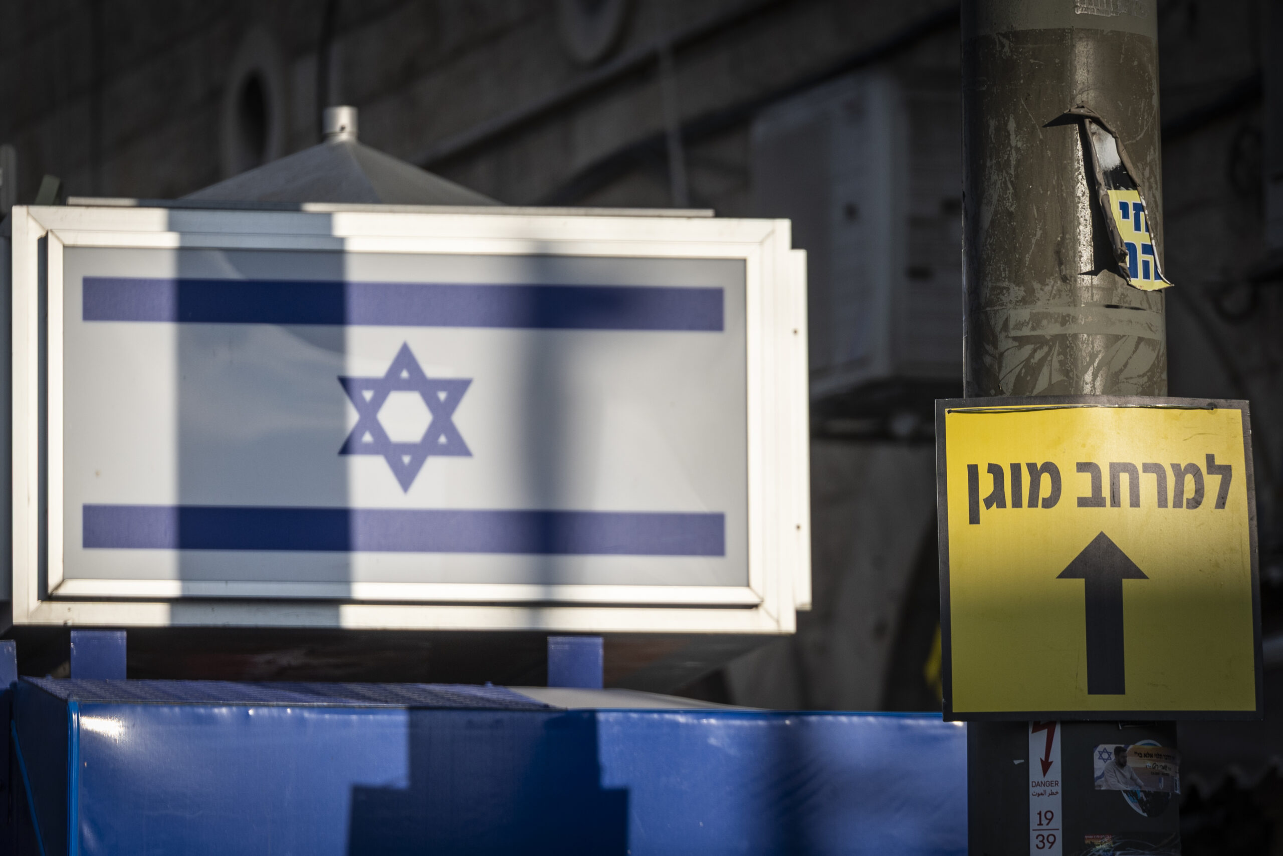 דגל ישראל נראה ליד שלט המצביע לעבר מרחב מוגן מחוץ לשוק מחנה יהודה בירושלים, על רקע המלחמה המתמשכת עם איראן וחיזבאללה וירי טילים לעבר ישראל, 9 במרץ 2026.